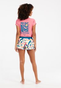 Top corto rosa con maniche corte e stampa grafica sul retro, abbinato a pantaloni da bagno colorati con motivi che presentano forme astratte e accenti tropicali.