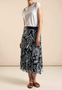 Spódnica w kwiatowy wzór w czarno-białe motywy, z lekkiego, płynącego materiału, z plisowanym krojem, uzupełniona gładką białą bluzką i brązowymi sandałami.