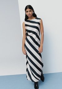 Vestido maxi sin mangas con rayas diagonales en negro y rosa pálido, hecho de una tela suave, con escote redondo y corte holgado.