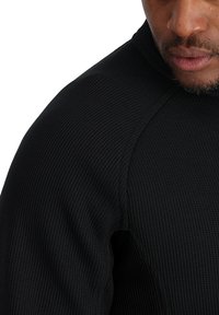 Felpa nera, texture lavorata con design a coste, colletto alto e maniche raglan, che mette in evidenza lo spessore e la vestibilità del tessuto.