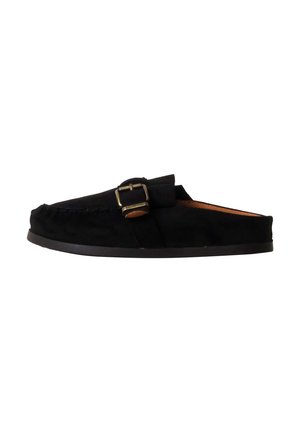 Mocassin en daim noir à enfiler avec boucle latérale et semelle basse en caoutchouc, vu de l’intérieur sur fond blanc.
