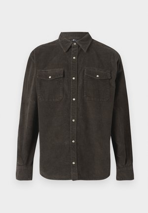 Camisa de pana marrón con cuello abotonado, manga larga, dos bolsillos en el pecho y herrajes plateados. Líneas verticales texturizadas por toda la prenda.