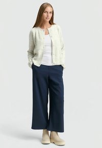 Ljus ribbad kofta i off-white, bärs över en vit topp, kombinerad med marinblå byxor med vida ben och beigea ankelboots. Enkel knappstängning.