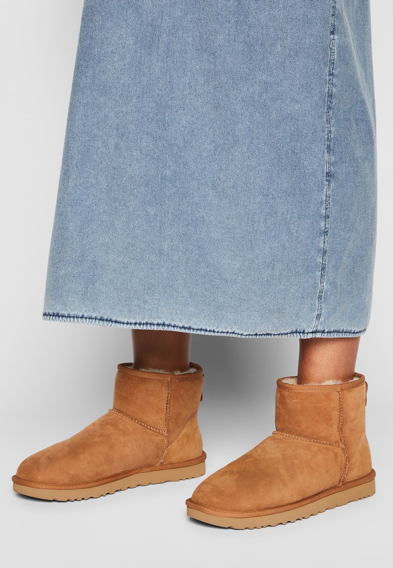 Stivaletti alla caviglia in suede beige con fodera morbida, punta curvata e suola testurizzata, abbinati a una gonna di jeans azzurro chiaro. Visibili dettagli delle cuciture.