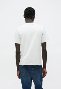 Ανοιχτό γκρι κο ντομάνικη μπλούζα με στρογγυλή λαιμόκοψη, απαλό βαμβακερό υλικό, φορεμένη με σκουρό μπλε τζιν παντελόνι που έχει πίσω τσέπες με λεπτομέρειες ραφής.