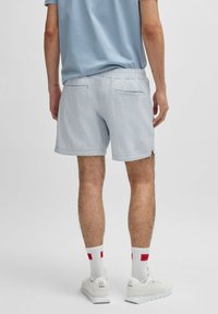 Lichtblauwe gestreepte shorts voor heren met een elastische tailleband, zijzakken en contrasterende witte schoenen met rode accenten en een logo op de sokken.