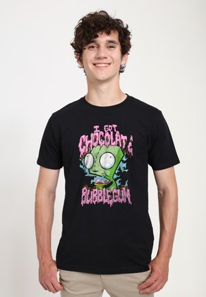 Jeune homme portant un t-shirt noir avec un personnage de dessin animé vert et un texte rose disant « I got chocolate bubblegum. »