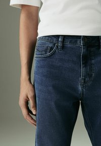 Jeans in denim blu scuro, con una vestibilità classica e un design a cinque tasche, cuciture visibili e chiusura con bottone in vita.