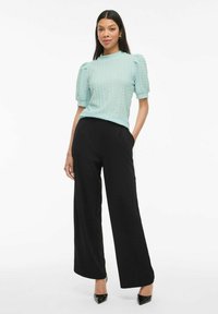 Top azzurro chiaro con texture e maniche corte a sbuffo, abbinato a pantaloni neri a vita alta con gambe ampie e décolleté neri a punta.
