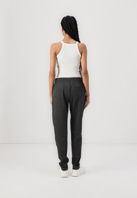 Tmavě šedé sportovní kalhoty se elastickým pasem a bočními kapsami, v kombinaci s bílým tílkem, viděné ze zadu. Hladká textilie.