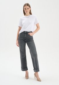 Biała koszulka z krótkim rękawem, ciemnoszare spodnie z wysokim stanem z podwiniętymi mankietami oraz beżowe buty na wysokim obcasie. Prosty design, casualowy wygląd.