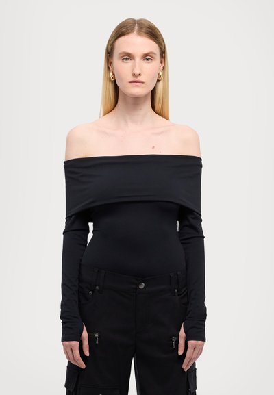 Schwarzer Body mit schulterfreiem Design, aus dehnbarem Stoff, mit langen Ärmeln, tailliertem Schnitt und subtilen Glanz, kombiniert mit schwarzen Cargo-Hosen.