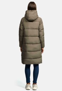 Zateplená olivovo zelená parka s kapucňou, s dlhým strihom, horizontálnym prešívaním a elastickými manžetami, skombinovaná s džínsami a teniskami.
