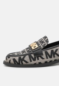 Mocassin à motif noir et beige avec impression du logo "MK", sangle en cuir noir et détail de boucle dorée sur la semelle plate.
