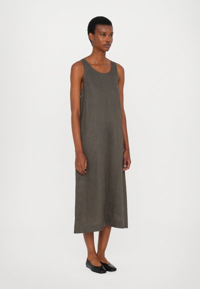 Uten ermer, ankel-lang kjole i mørk olivengrønn lin med en avslappet passform og sidespalter. Bært med svarte flate sko.