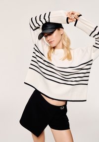 Maglione a righe crema e nero con maniche ampie abbinato a una gonna avvolgente nera con accento di bottone. Silhouette e texture moderne.