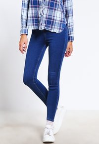 Úzké modré džíny z denimu s hladkou texturou, s pasem ve střední výšce a přiléhavým střihem, doplněné kostkovanou košilí na knoflíky.