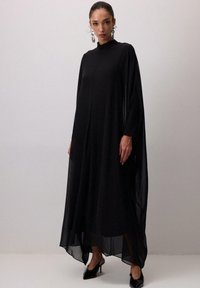 Must must rõivastus musta kappa stiilis, millel on pikad varrukad, kõrge kaelus ja läbipaistev kangas. Omab vabalt mõõdetud lõiget ja ebatasast hemmi, sobita teravapatjadega kingadega.