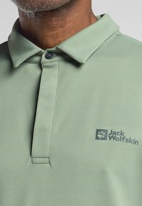Lichtgroen polo shirt gemaakt van een gestructureerd materiaal, met een knoopsluiting bij de kraag en het Jack Wolfskin-logo op de borst.