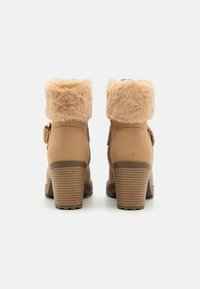 Tan ankle boots with faux fur trim at the top, sturdy block heel, textured sole, and decorative side buckle detail.