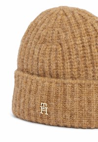 Gebreide beanie in een warme, bruine tint met een textuur van ribbels. Bevat een gouden logo-accent op de opgevouwen manchet. Zacht materiaal dat aan wol doet denken.