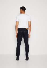 Jeans de mezclilla azul oscuro con una textura suave, diseño ajustado y costuras en naranja contrastante; combinados con una camiseta blanca de manga corta.