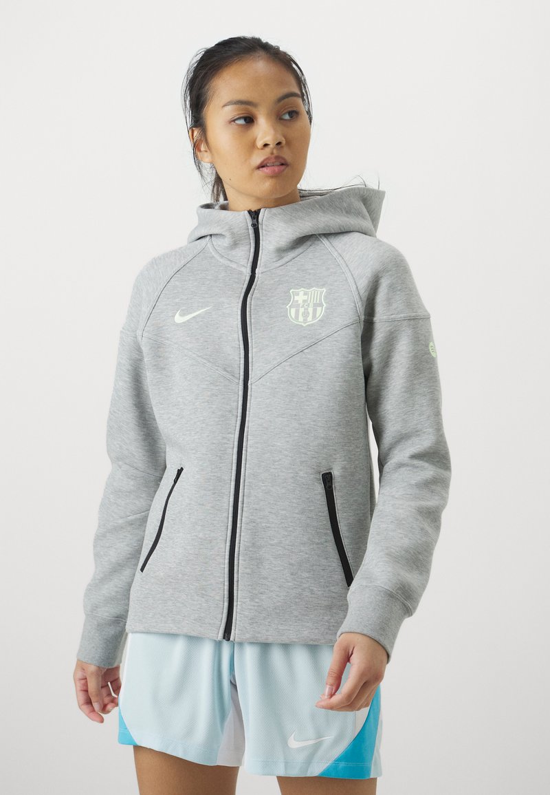 Szara bluza z kapturem na pełny zamek, z kontrastowym kapturem, czarnymi kieszeniami na zamek błyskawiczny oraz logo Barcelony na lewej piersi.