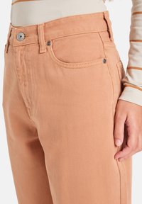 Pantalones de mezclilla de color melocotón con un diseño clásico de cinco bolsillos, costuras en contraste y un cierre de botón metálico en la cintura.