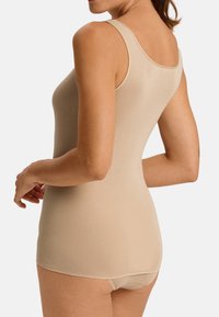 Top beige senza maniche con spalline sottili, design aderente, texture morbida, schiena senza cuciture e taglio corto alla base, adatto per essere indossato a strati.