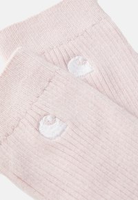 Chaussettes en tricot rose pâle avec texture côtelée et détail du logo blanc brodé sur le bord. Fini lisse avec une apparence douce.