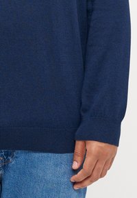 Mörkblå stickad tröja med rund halsringning och ribbade ärmslut. Mjuk textur, figursydd vid midjan, kombinerad med ljusa denimjeans.