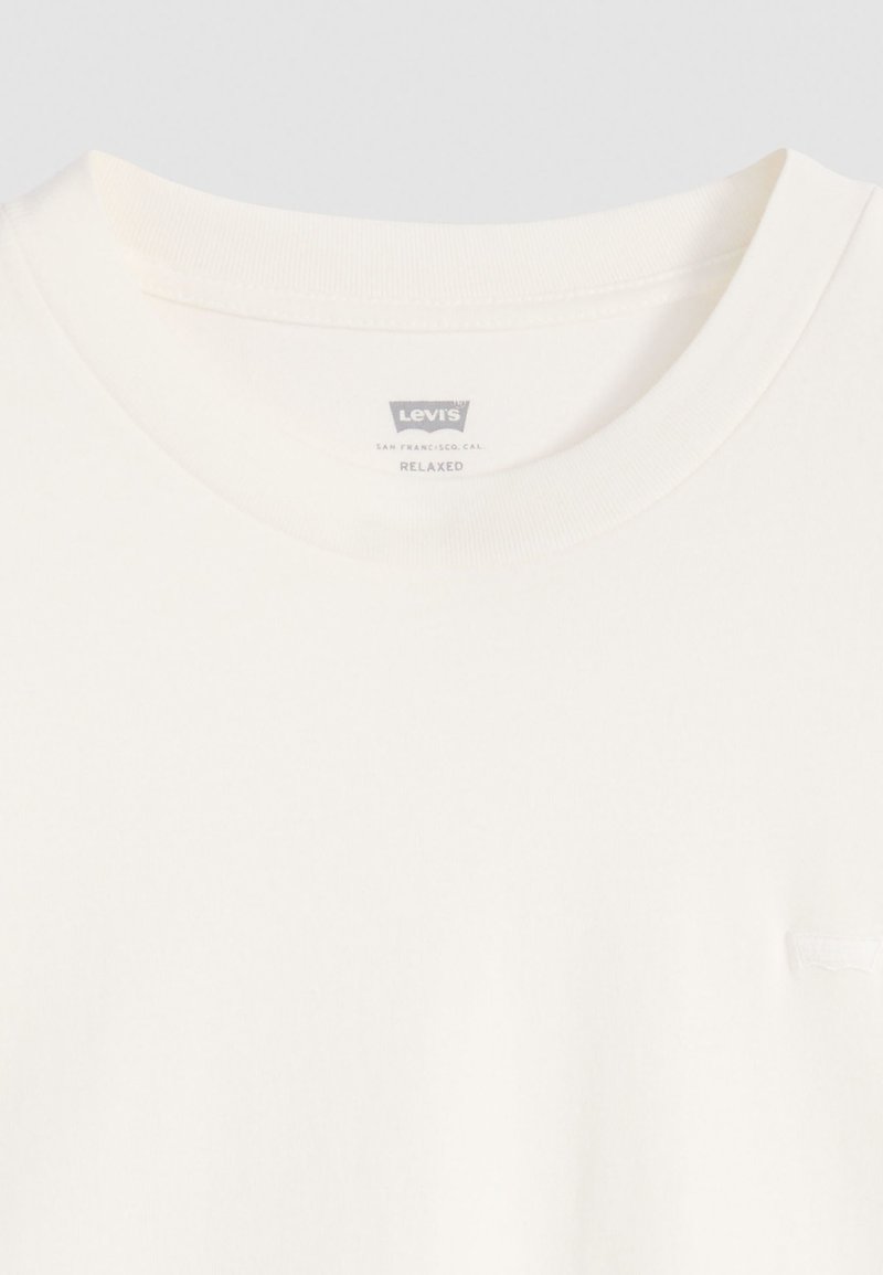 Luźna koszulka w kolorze kremowym z okrągłym dekoltem oraz małą, dyskretną metką z logo przy kołnierzyku. Wykonana z miękkiego materiału bawełnianego.