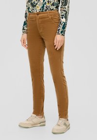 Bruine corduroy broek met een rechte pasvorm, voorzien van zakken aan de voorkant en een knoopsluiting, gecombineerd met lichtgekleurde sneakers.