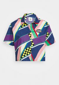 T-shirt cropped présentant un mélange de motifs géométriques bleus, roses, verts et jaunes avec un logo noir et blanc de Vans sur la poitrine.