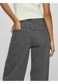 Šedé široké džíny s texturovaným povrchem, které mají dvě zadní kapsy a vysoký pas. Látka vypadá pevně a připomíná denim.