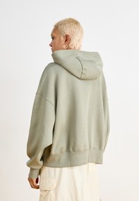 Sweatshirt com capuz oversized em tecido verde suave. Apresenta punhos e bainha canelados, com um corte descontraído e uma textura suave e aveludada.