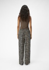 Vide ben bukser i leopardmønster i tan, sort og creme farve, med høj talje og løs pasform. Bæres med en brun ærmeløs top.