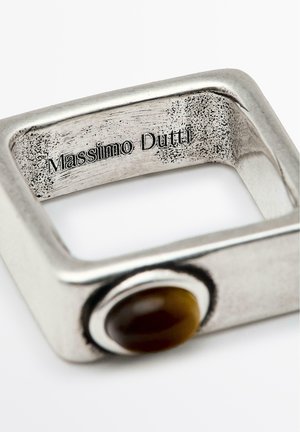 Bague en métal carré avec une finition argentée brossée. Présente un accent en pierre brune ronde d'un côté et une marque gravée à l'intérieur.