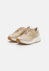 Beige tenisky s texturovaným povrchem, s robustní bílou mezipodešví, jemnými metalickými akcenty a zaobleným designem špičky.
