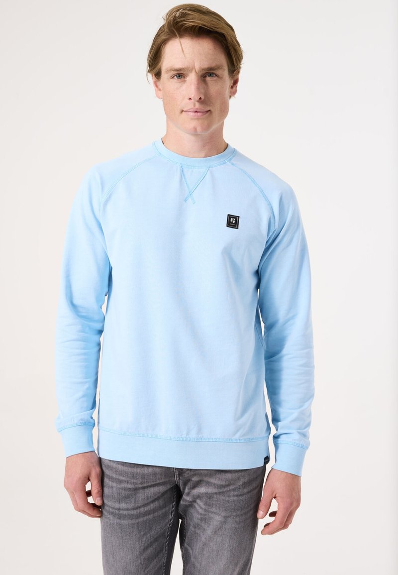 Sudadera azul clara de tela suave, con cuello redondo, mangas largas y un pequeño parche de logo negro en el pecho.
