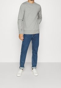 Szara bluza z ribbowymi mankietami i dołem, w połączeniu z niebieskimi dżinsami. Białe sneakersy dopełniają stylizację. Prosty design, luźny krój.