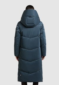 Tmavě modrozelená péřová bunda s kapucí, zdobená vzorem ve tvaru šipek, s dlouhým střihem a logem u lemu. Hladká, lesklá textura.