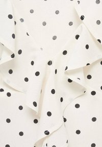 White blouse with black polka dots, featuring ruffles along the neckline. The fabric appears lightweight with a smooth texture.