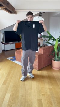 Polo nero sollevato, con colletto e maniche corte. Etichetta attaccata. Design semplice, esposto su uno sfondo interno chiaro.