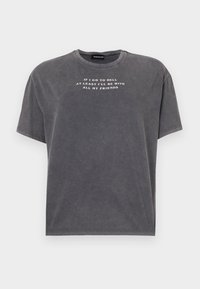 Šedé oversized tričko vyrobené z měkké látky, se širokým výstřihem a krátkými rukávy, s bílým potiskem na přední straně.