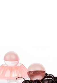 Des pots ronds roses de masque pour les lèvres avec une finition brillante, étiquetés "Abib", placés sur une assiette à dessert rose entourée de cerises noires.