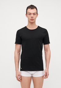 T-shirt nera a girocollo in cotone, maniche corte, design aderente, con un piccolo dettaglio del logo verde all'orlo.