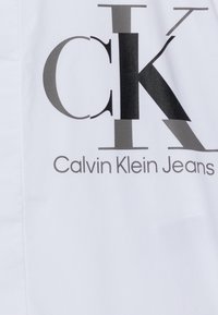 Calvin Klein Jeans logo with large overlapping "ck" letters in black and gray on white fabric.