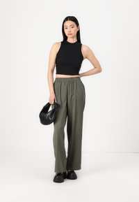 Haut court sans manches noir, pantalon large vert olive, et sac à main noir. Matériaux doux, coupe décontractée et taille élastique.