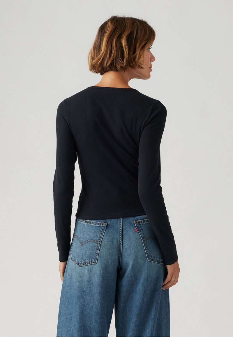 Haut noir à manches longues avec texture côtelée et encolure ronde, associé à un jean en denim bleu clair à jambes larges avec poches arrière.